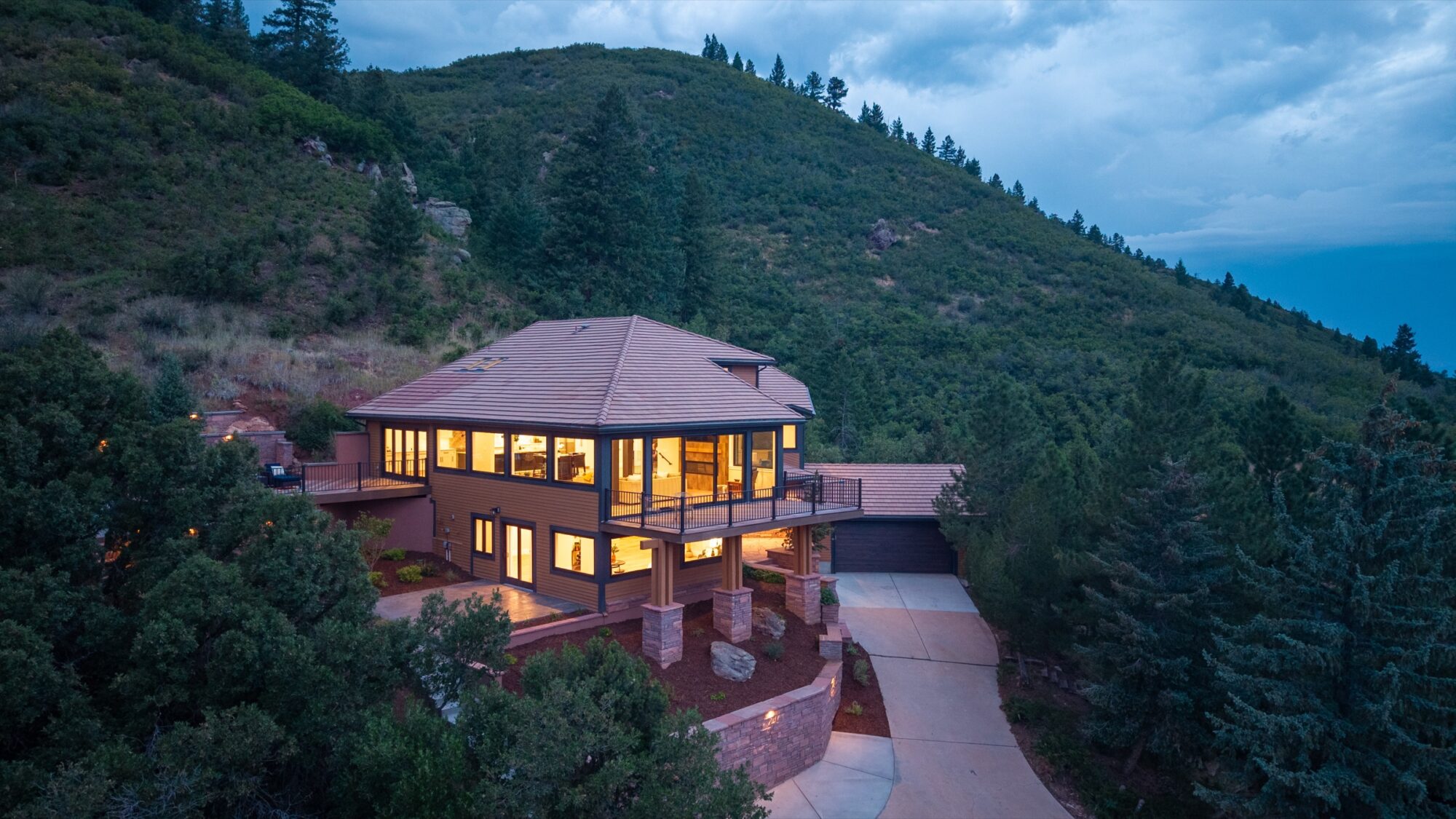 Wide aerial dusk view of a mountainside home with Jet Black Win-Dor windows and sliding patio door lit from inside.